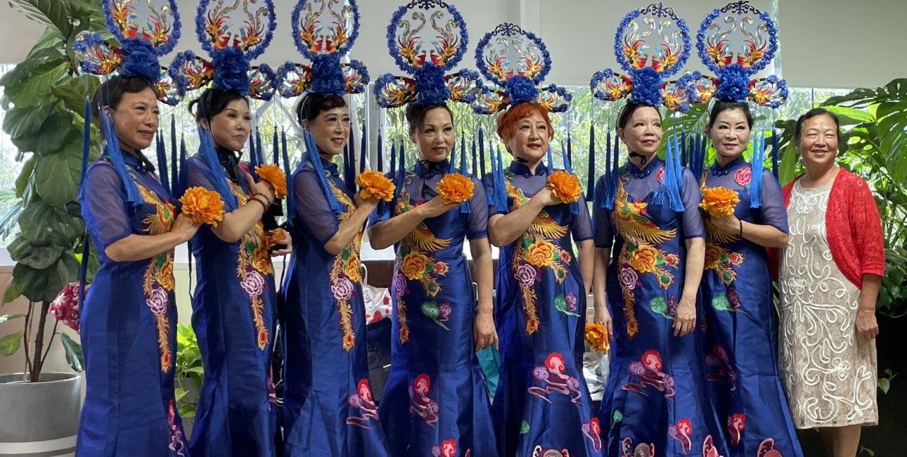 Women in traditional blue attire perform at a cultural event supported by Metro Assist.
